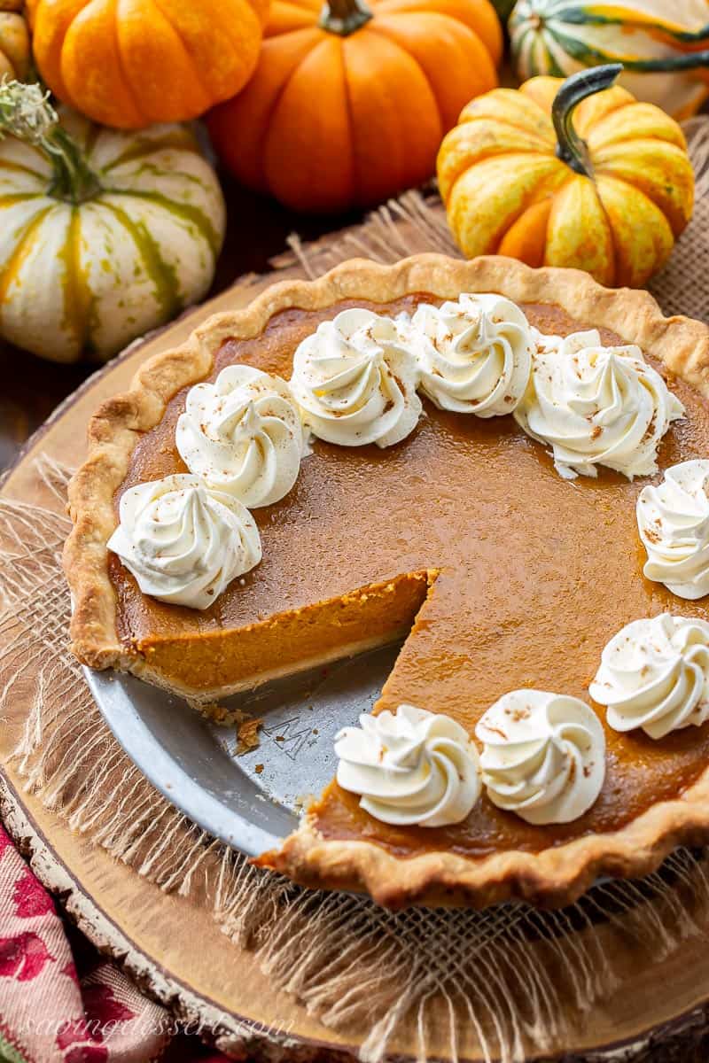 A pumpkin pie with one slice removed. Topped with swirls of whipped cream