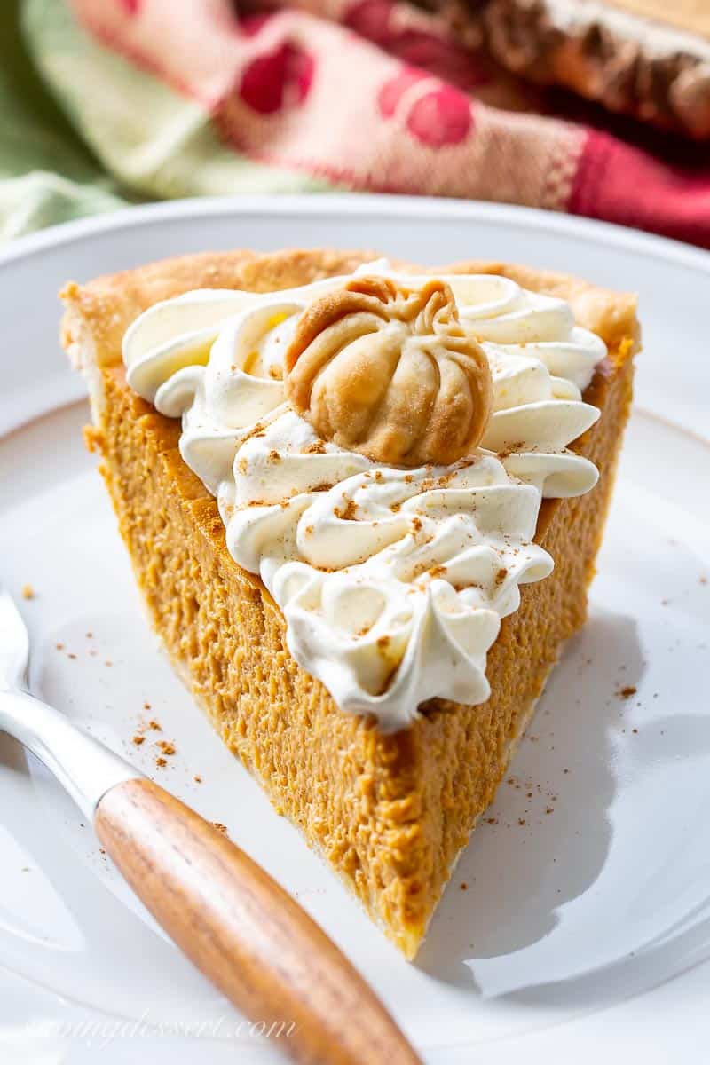 A slice of pumpkin pie topped with whipped cream and a pumpkin shaped crust cookie