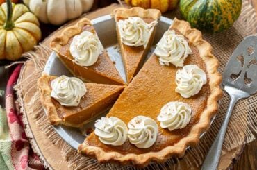 Sliced pumpkin pie decorated with whipped cream swirls