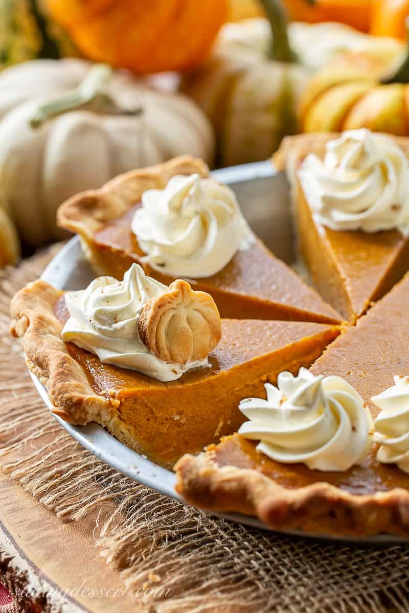 Side view of a sliced pumpkin pie with swirls of whipped cream and a pumpkin cut-out crust cookie