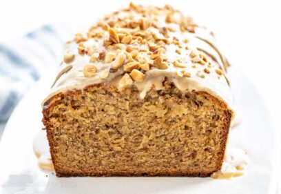a side view of a sliced loaf of banana bread topped with peanut butter icing and chopped peanuts