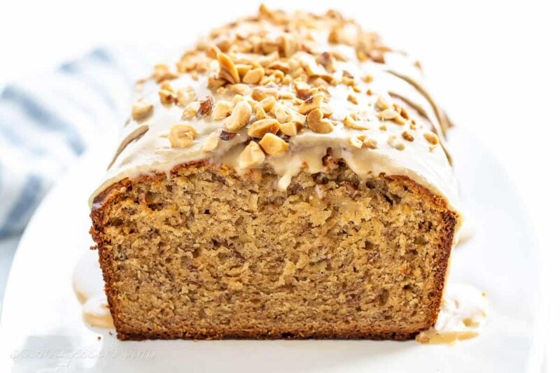 a side view of a sliced loaf of banana bread topped with peanut butter icing and chopped peanuts