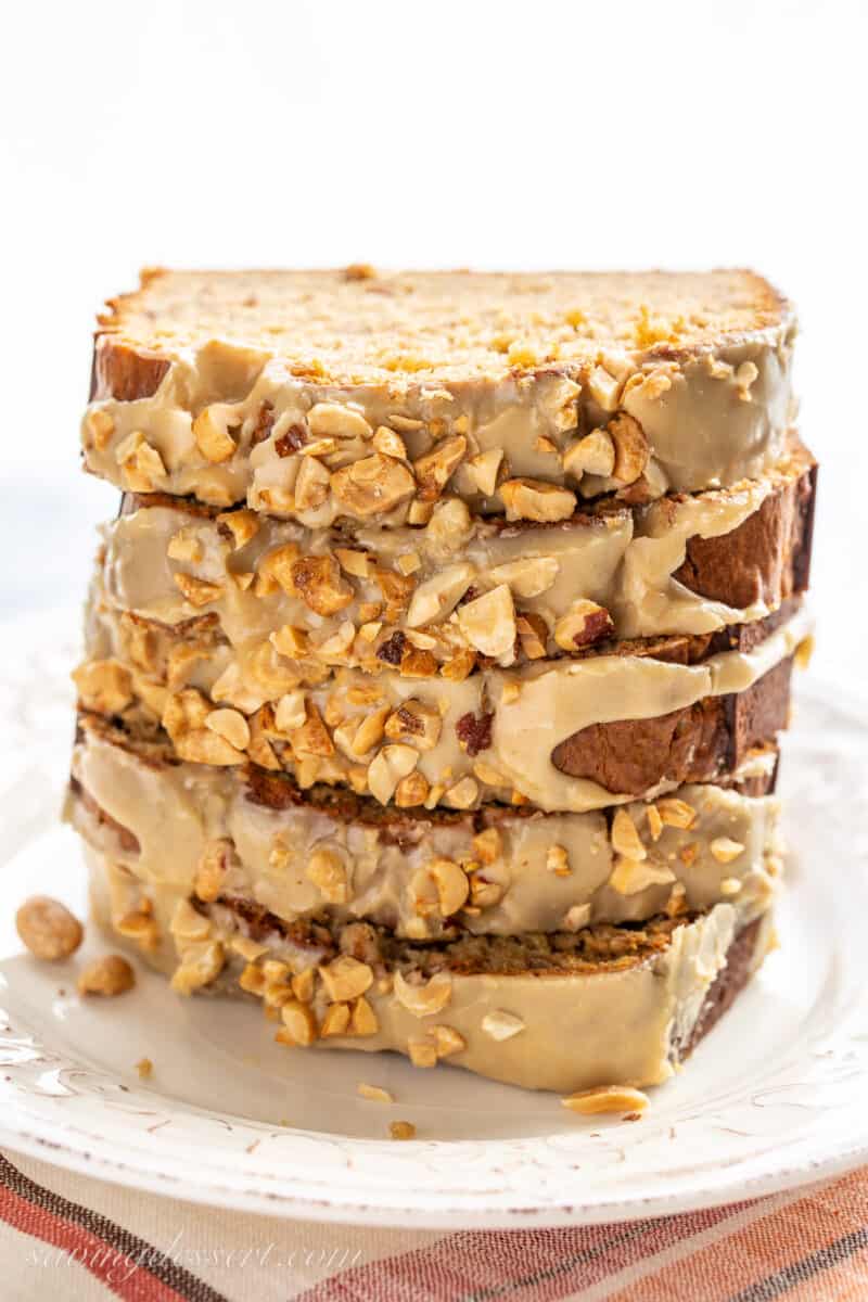 a stack of sliced peanut butter banana bread with a peanut butter glaze topped with chopped peanuts