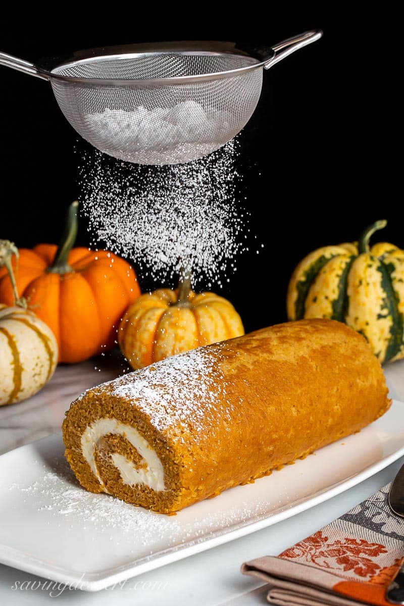 A pumpkin roll being covered with powdered sugar from a sifter