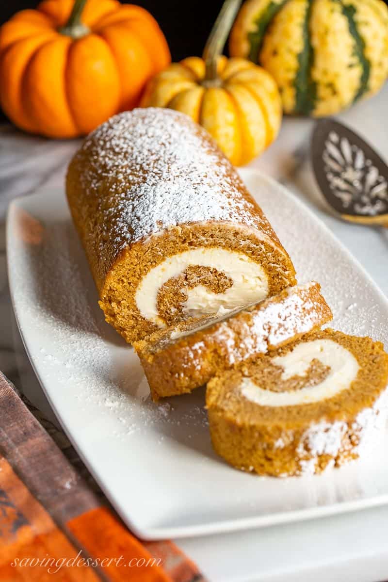 Sliced pumpkin roll on a platter with decorative pumpkins in the background