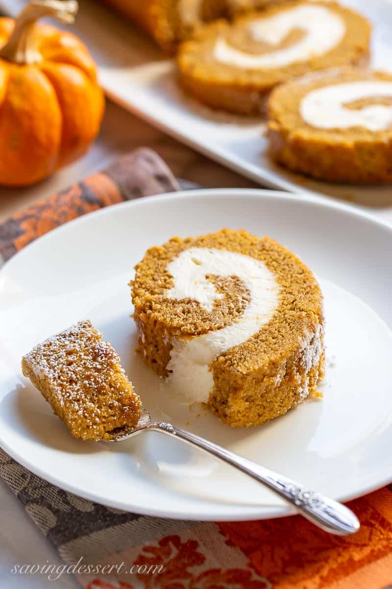 Side view of a thick slice of pumpkin roll with cream cheese filling and a fork
