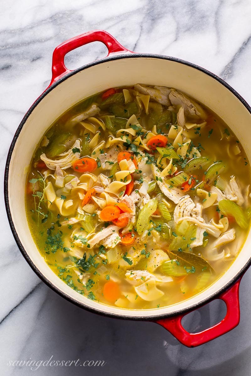 A Dutch oven filled with chicken noodle soup with carrots and celery