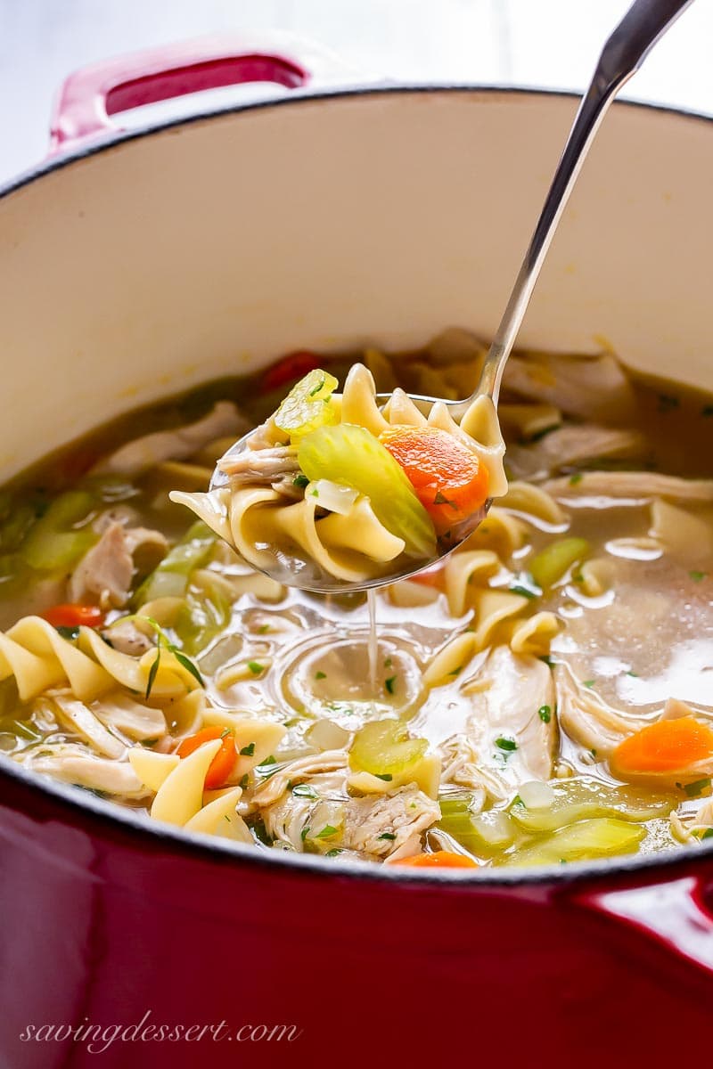 A ladle filled with noodles, carrots and chicken