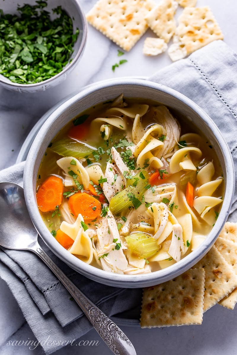 A bowl of chicken noodle soup served with crackers and garnished with parsley