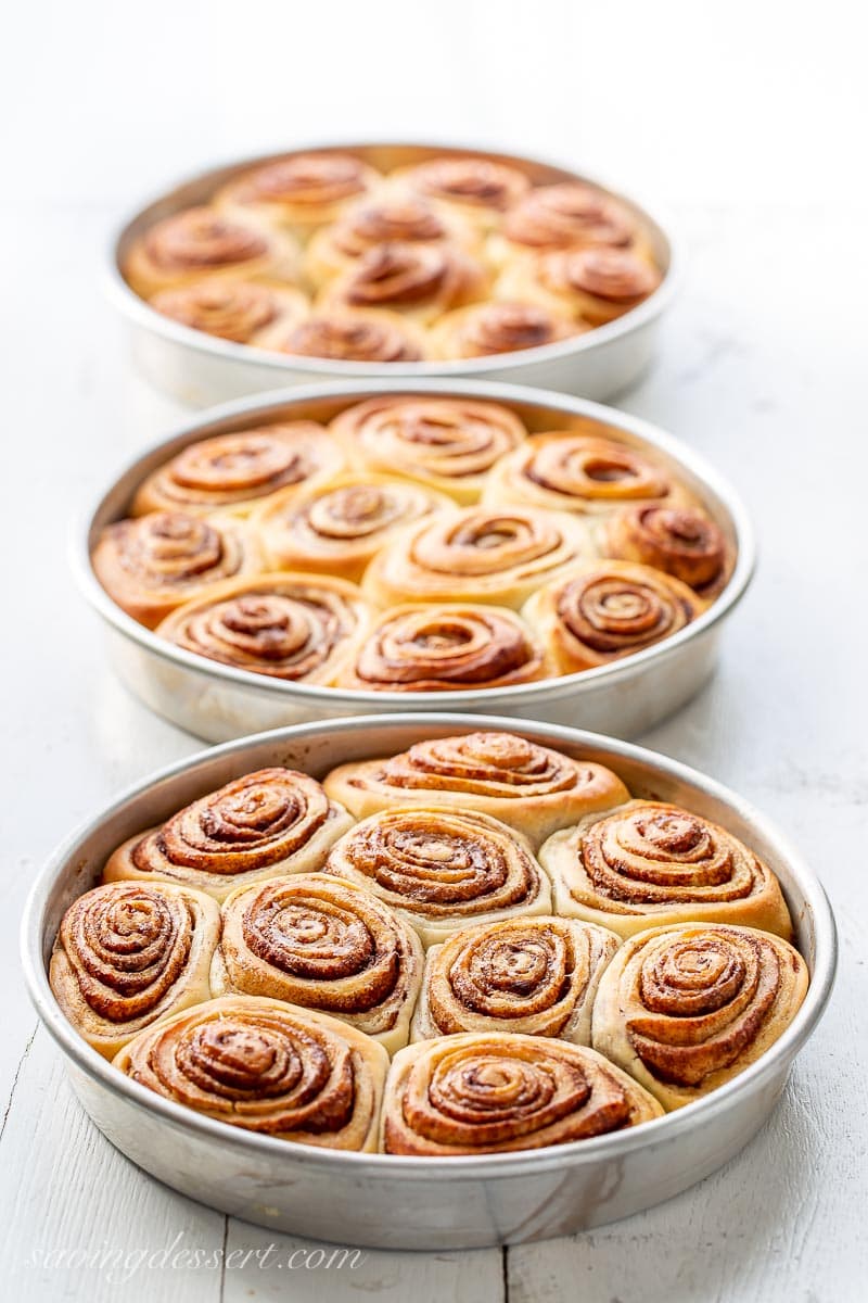 Three pans of baking cinnamon rolls, no frosting