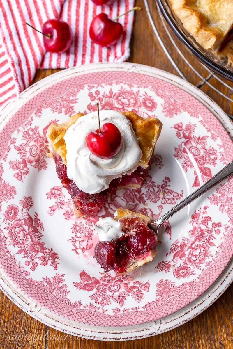 An overhead photo of a slice of pie topped with whipped cream and a cherry