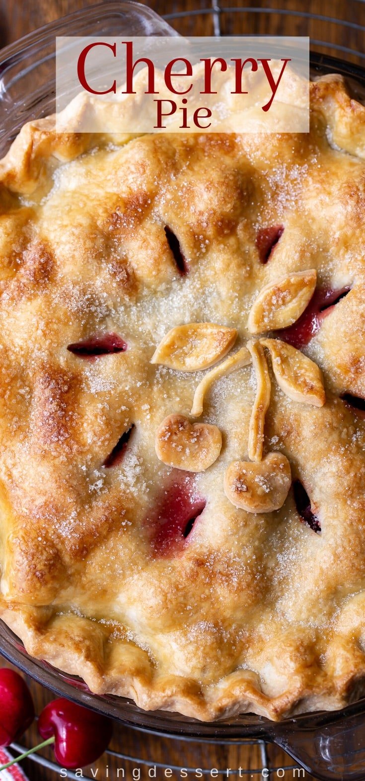 A closeup of a baked pie with a golden brown top crust decorated with pastry cut-outs in the shape of cherries and leaves