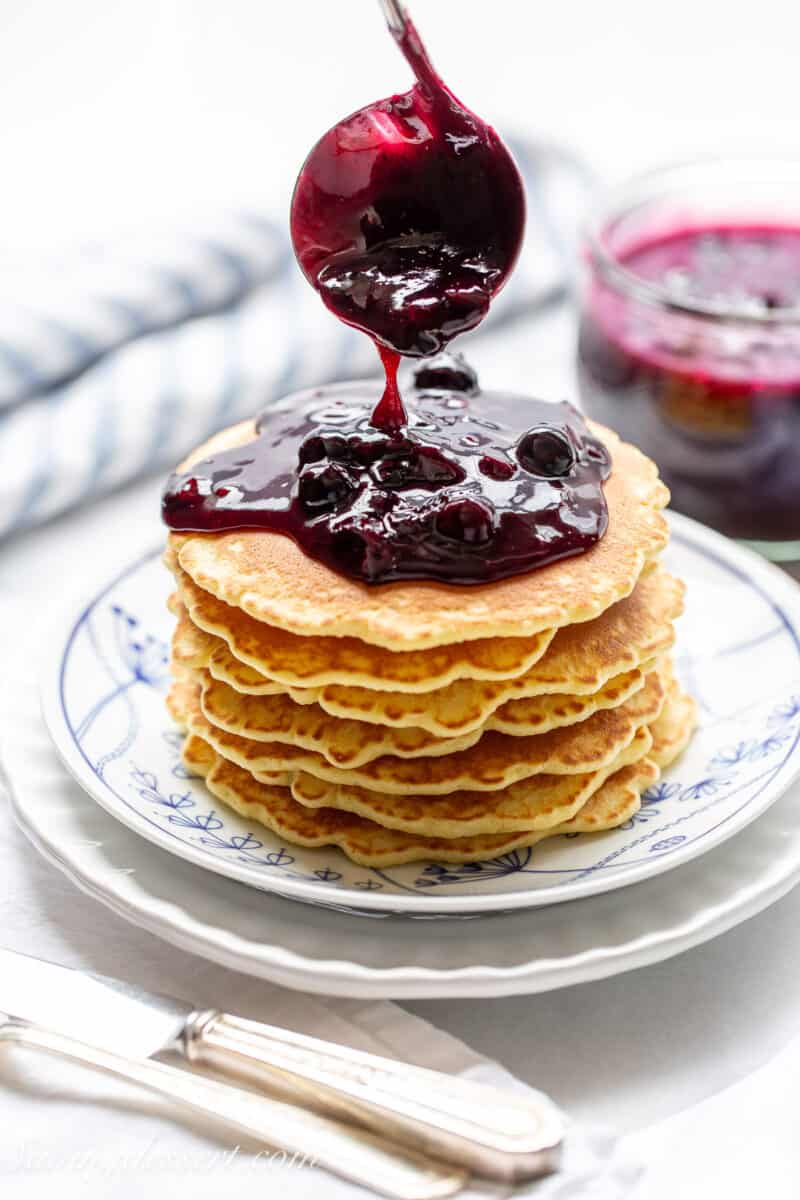 A stack of pancakes being drizzle with spoonfuls of blueberry sauce