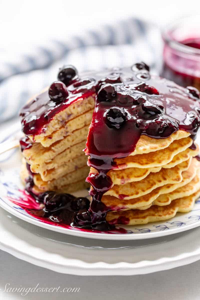 a stack of pancakes with a slice taken out and blueberry sauce dripping down the sides