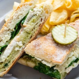An overhead view of a sliced chicken panini sandwich with a pickle on top and chips on the side.