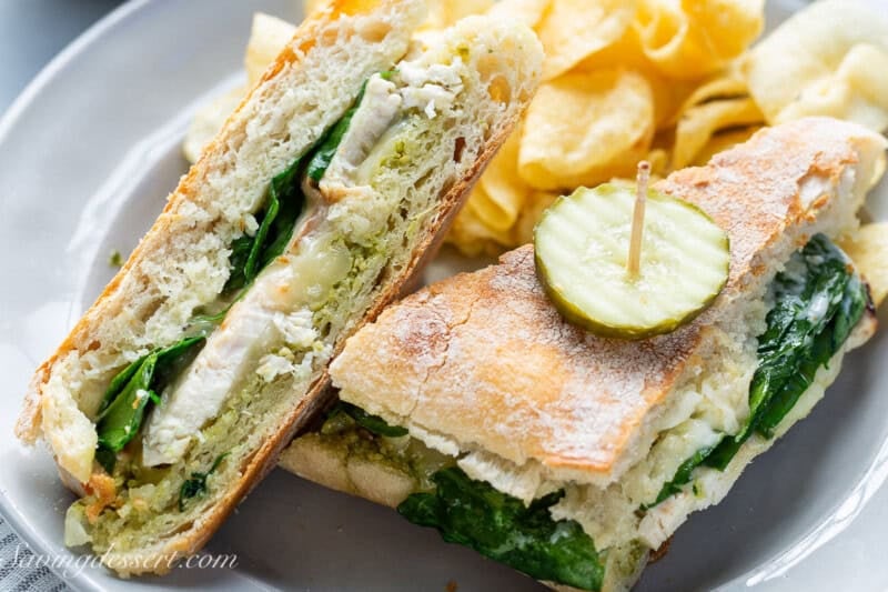 An overhead view of a sliced chicken panini sandwich with a pickle on top and chips on the side.