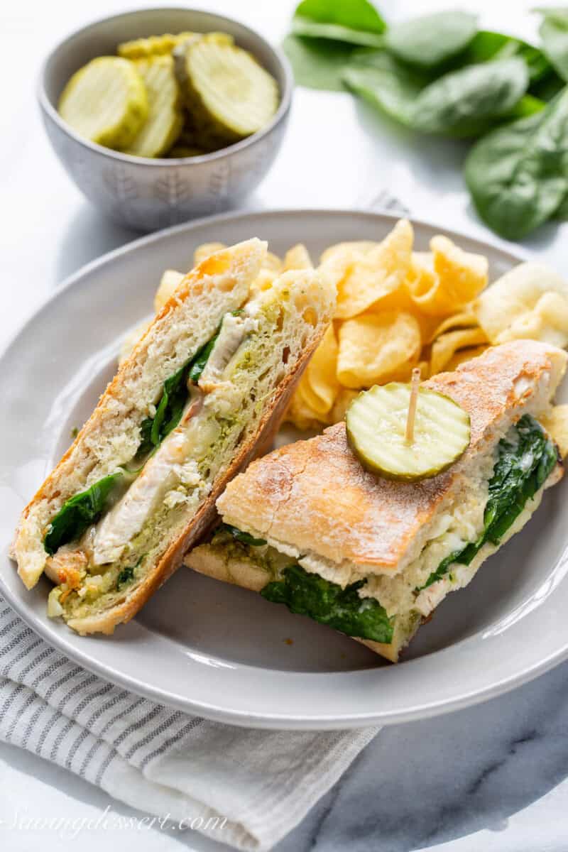 A chicken panini sandwich on a plate with chips and pickles.
