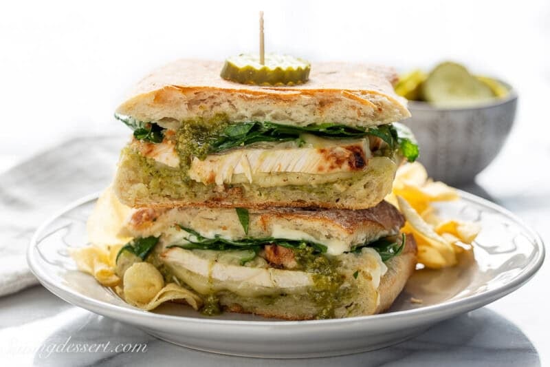 A stacked chicken pesto panini sandwich topped with a pickle slice.