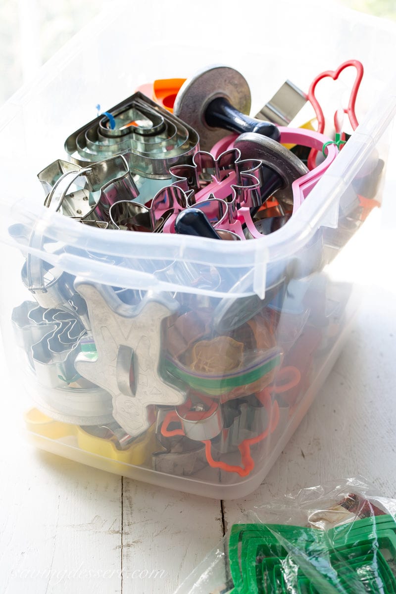 A clear container filled with a wide variety of cookie cutters used when making a cut-out sugar cookie recipe