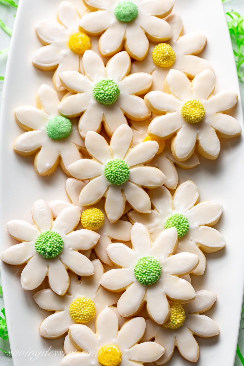 A tray of sugar cookies shaped like flowers simply iced and decorated with green and yellow middles