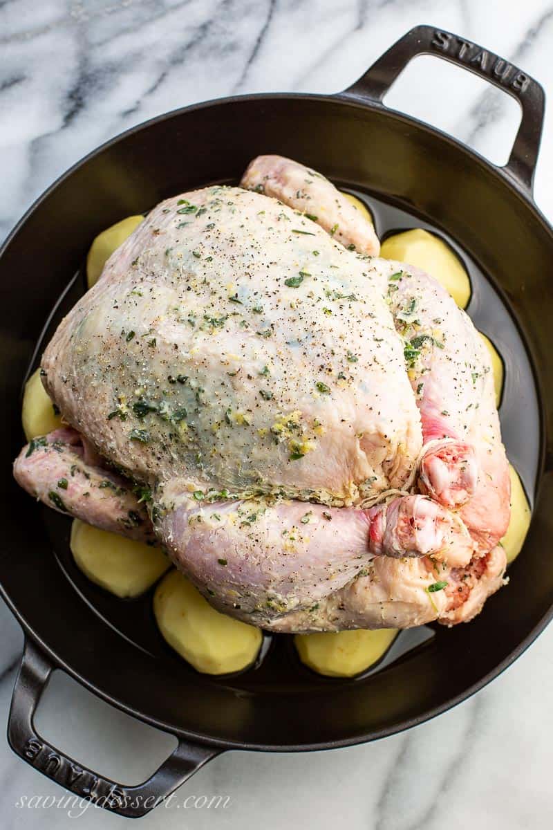 An un-roasted chicken sitting on potatoes in a large skillet