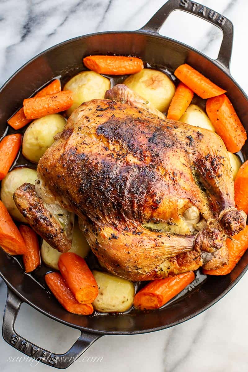 Roasted chicken in a large skillet sitting over potatoes and carrots