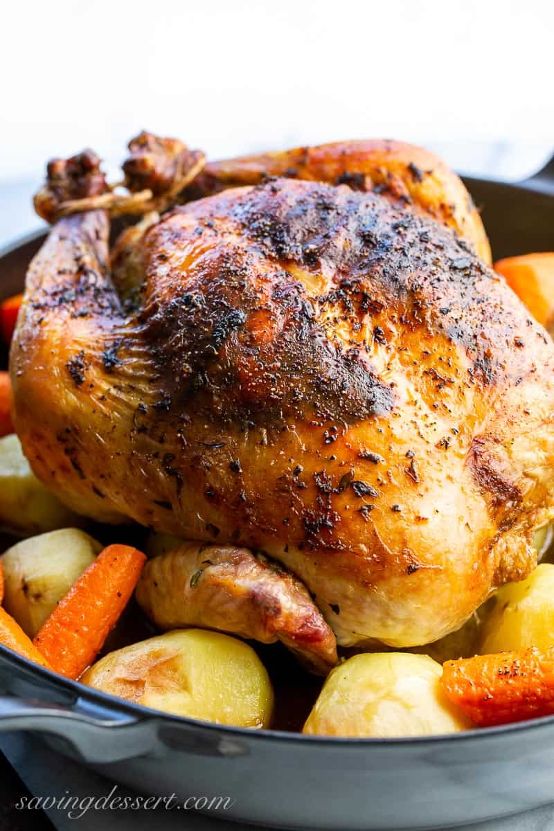 A side view of a whole roast chicken with potatoes and carrots