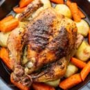 Overhead view of a whole roast chicken with carrots and potatoes in a skillet