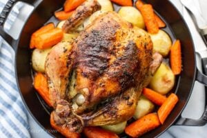 Overhead view of a whole roast chicken with carrots and potatoes in a skillet