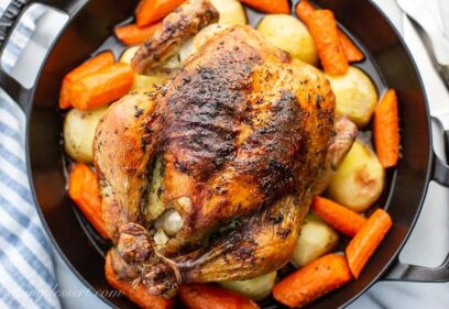 Overhead view of a whole roast chicken with carrots and potatoes in a skillet