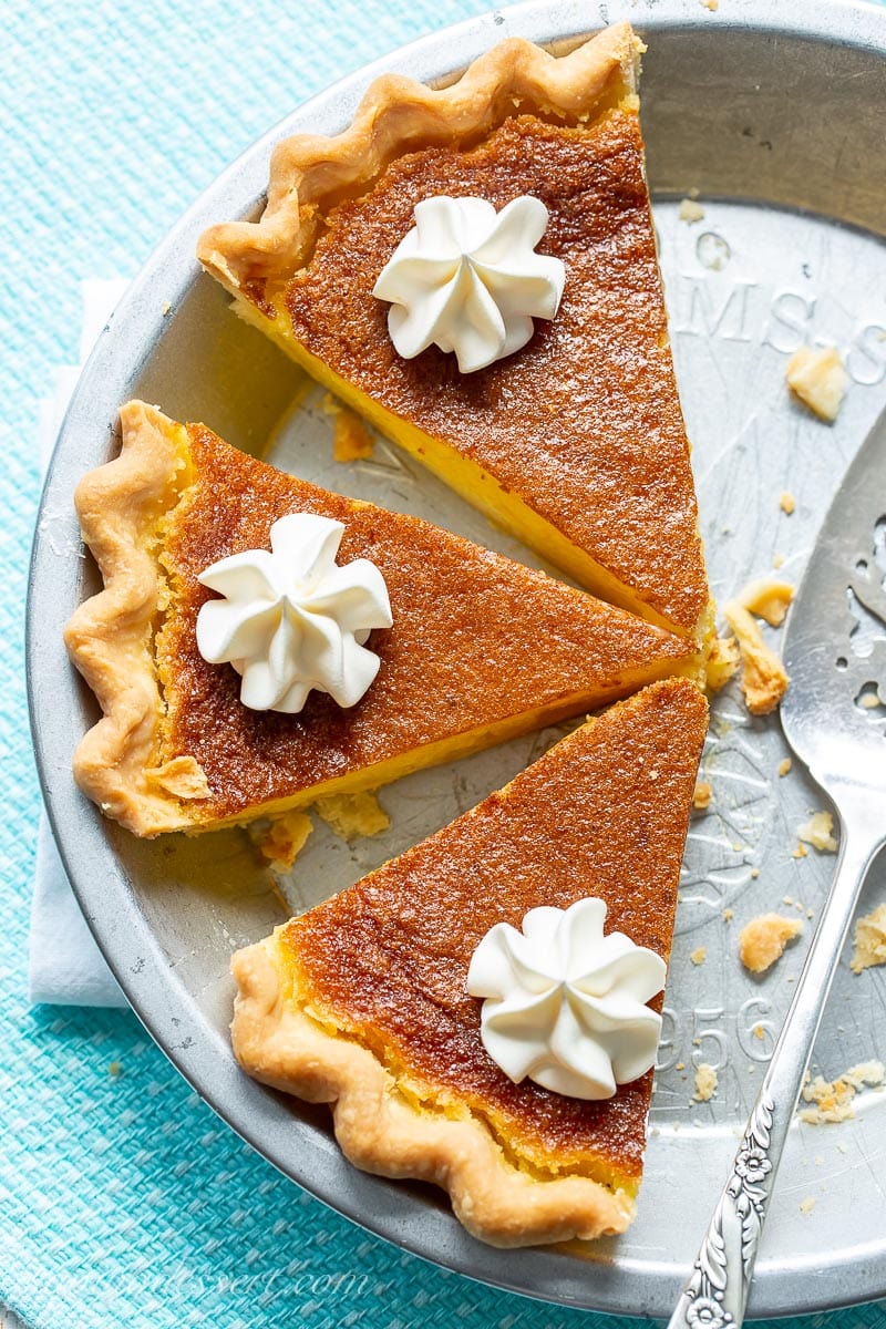 An overhead view of a sliced lemon pie with a golden brown top with swirls of whipped cream on each slice