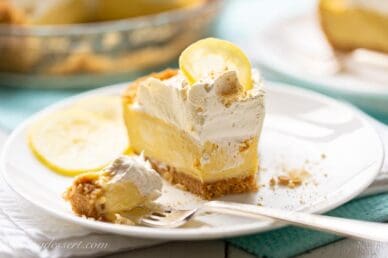 a partially eaten slice of lemon icebox pie on a plate with whipped cream and a lemon slice on top