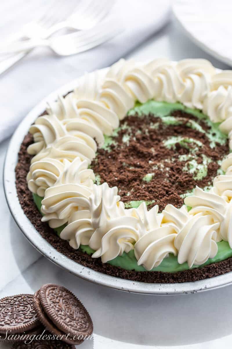 A side view of a Grasshopper Pie decorated with swirls of whipped cream and crushed Oreo cookies
