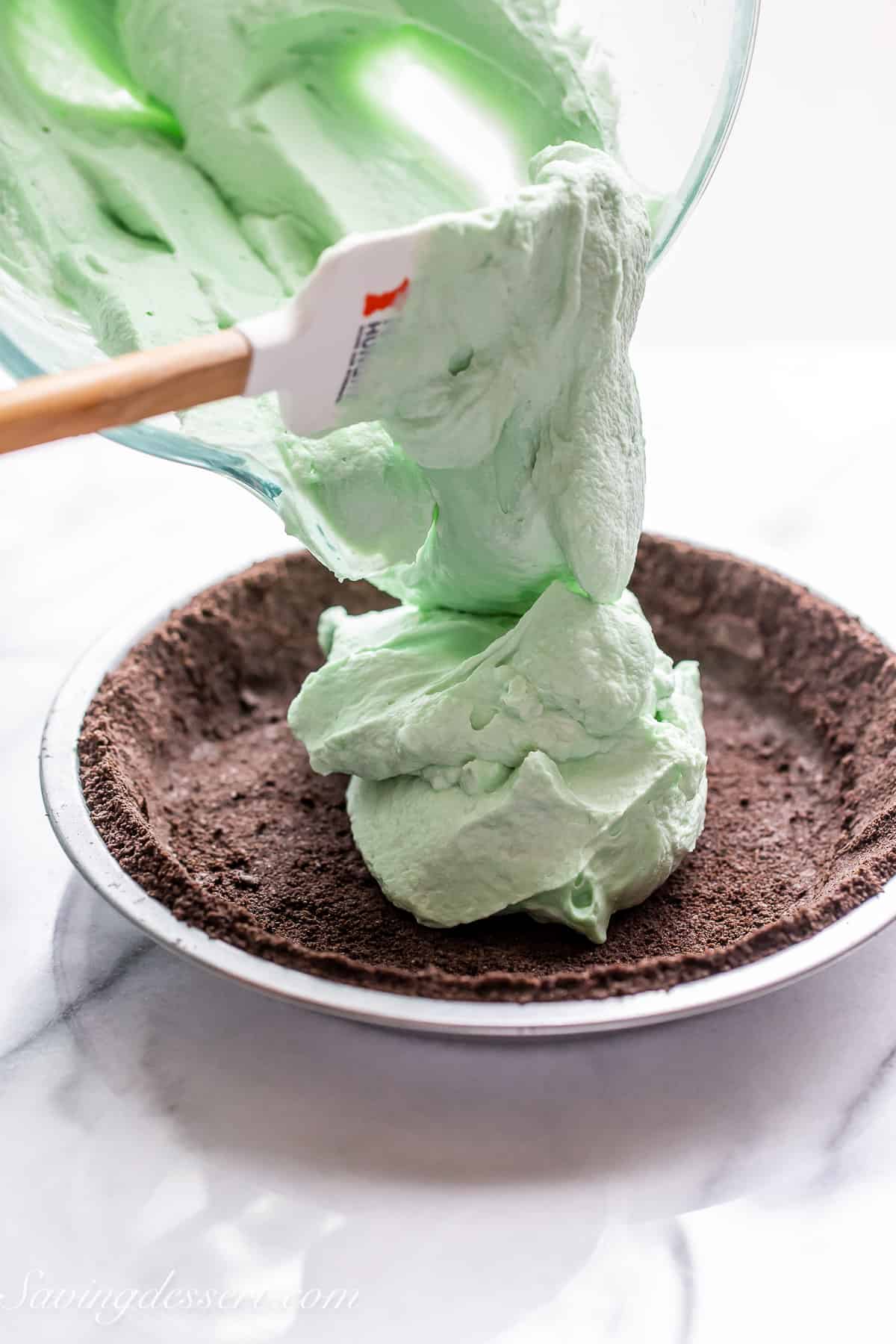 an oreo cookie crust being filled with fluffy light green pie filling