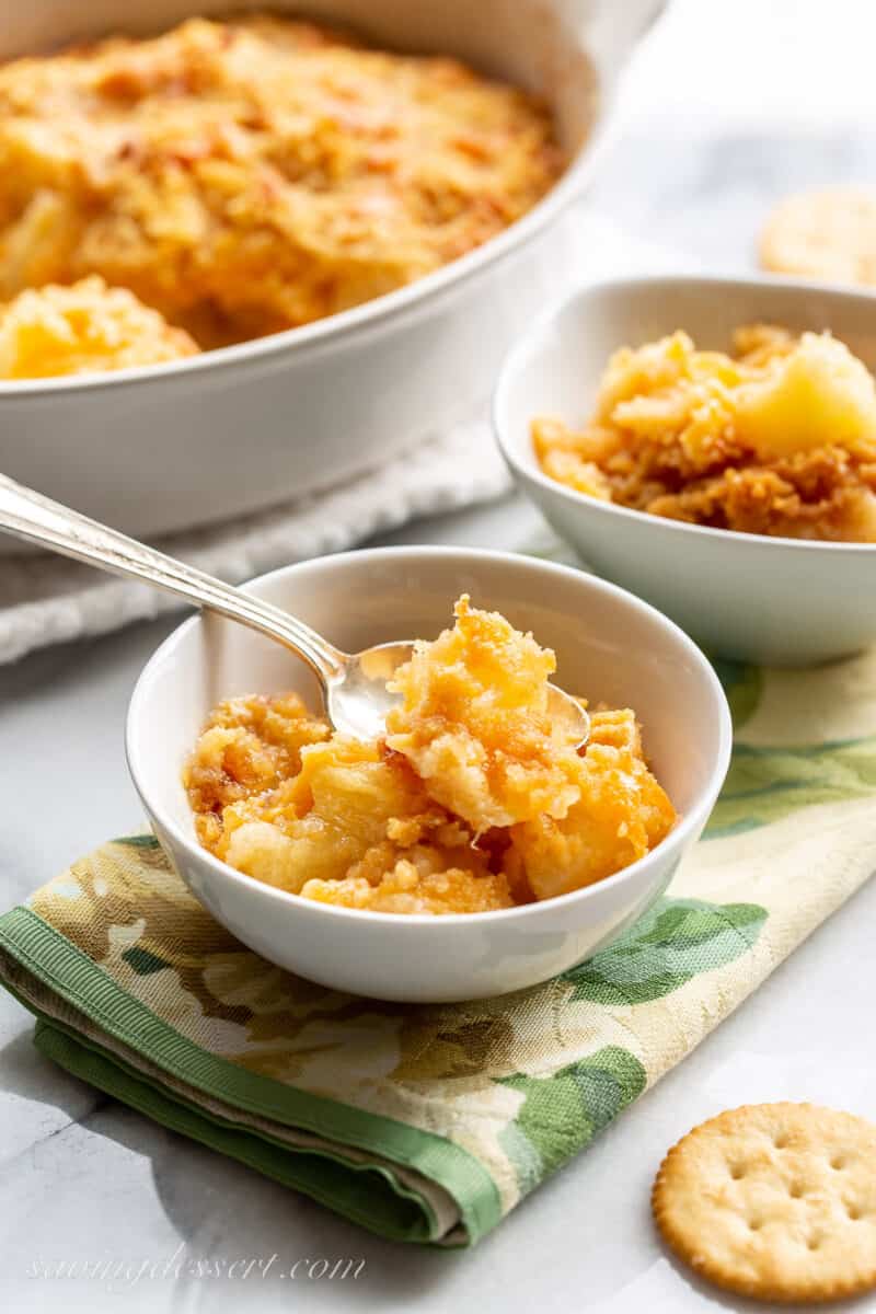 a bowl of hot pineapple casserole with a spoon and Ritz crackers