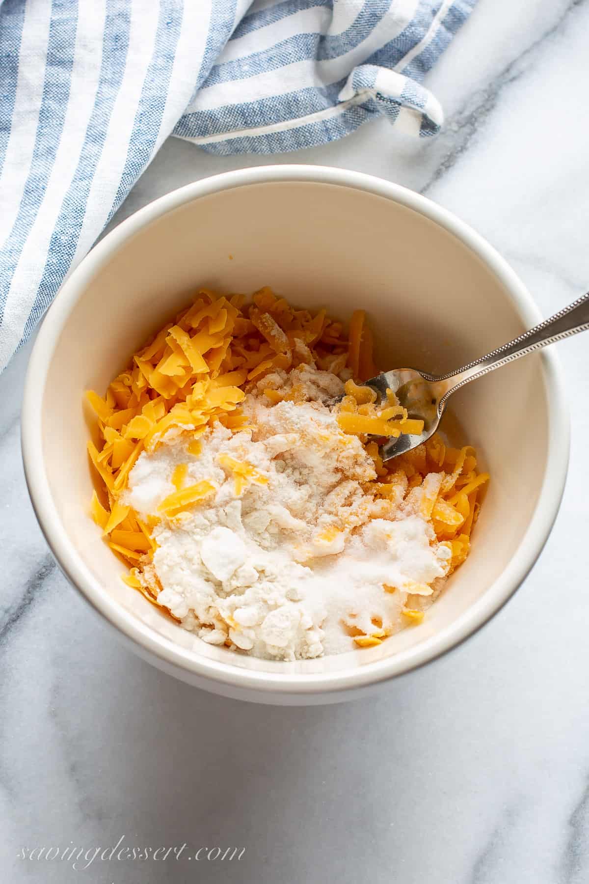 A small bowl with shredded cheddar cheese, sugar and flour