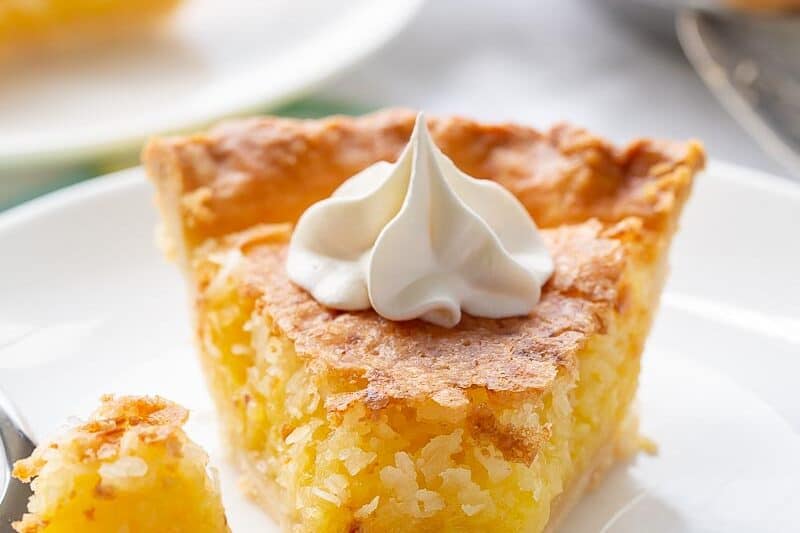 A slice of French coconut pie on a plate topped with whipped cream