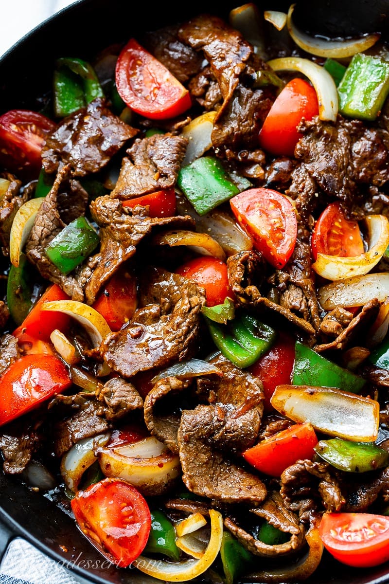 A closeup of a skillet with thin strips of steak with chunks of peppers, onions and tomatoes