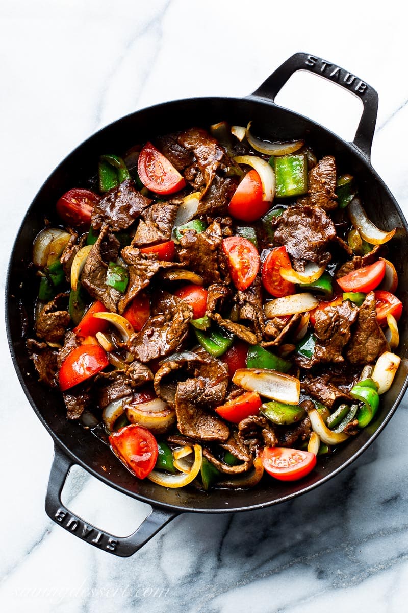 A skillet filled with thin strips of steak, peppers, onions and tomatoes