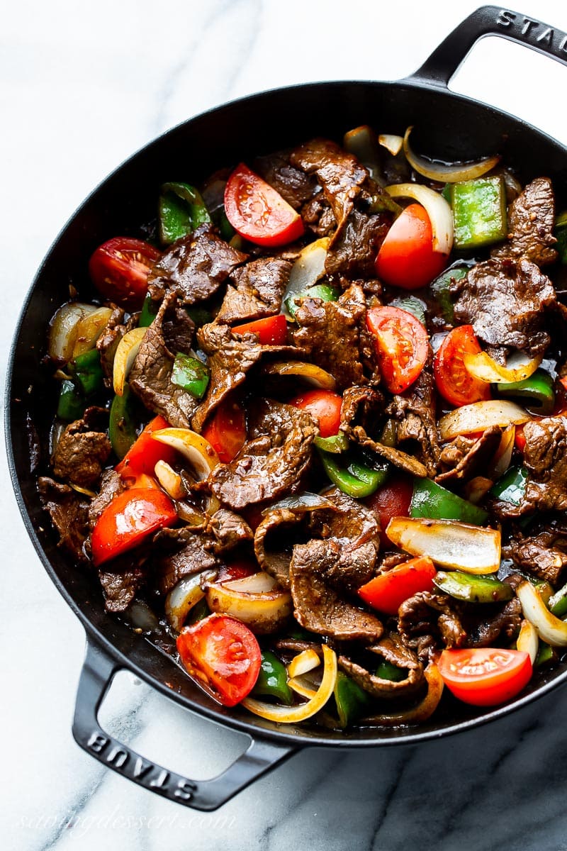 A skillet filled with steak, peppers, onions and tomatoes in a soy based sauce