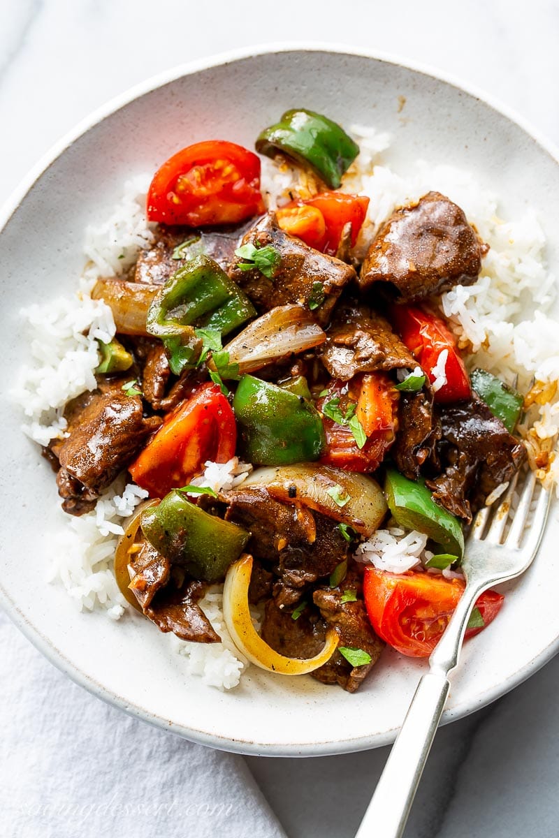 A bowl of rice topped with green pepper steak with tomatoes