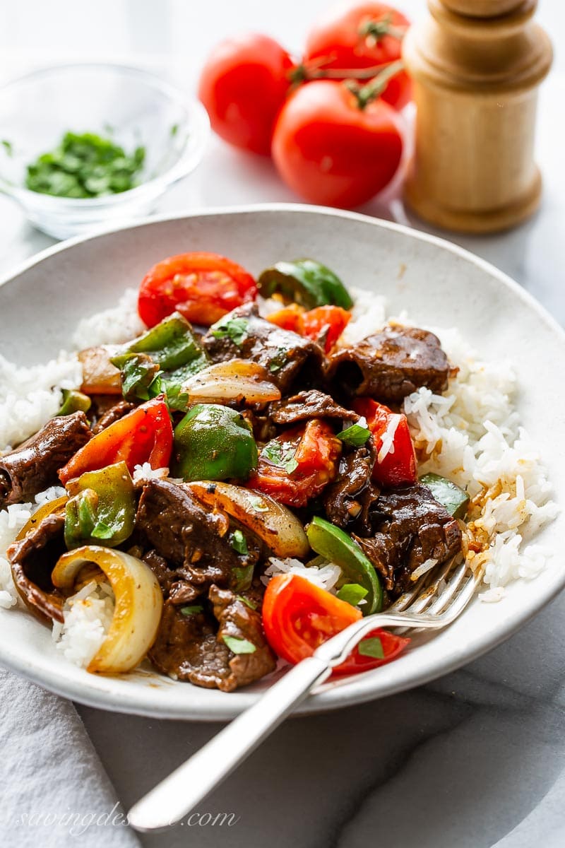 A big bowl with rice, pepper steak, onions, peppers and tomatoes garnished with parsley