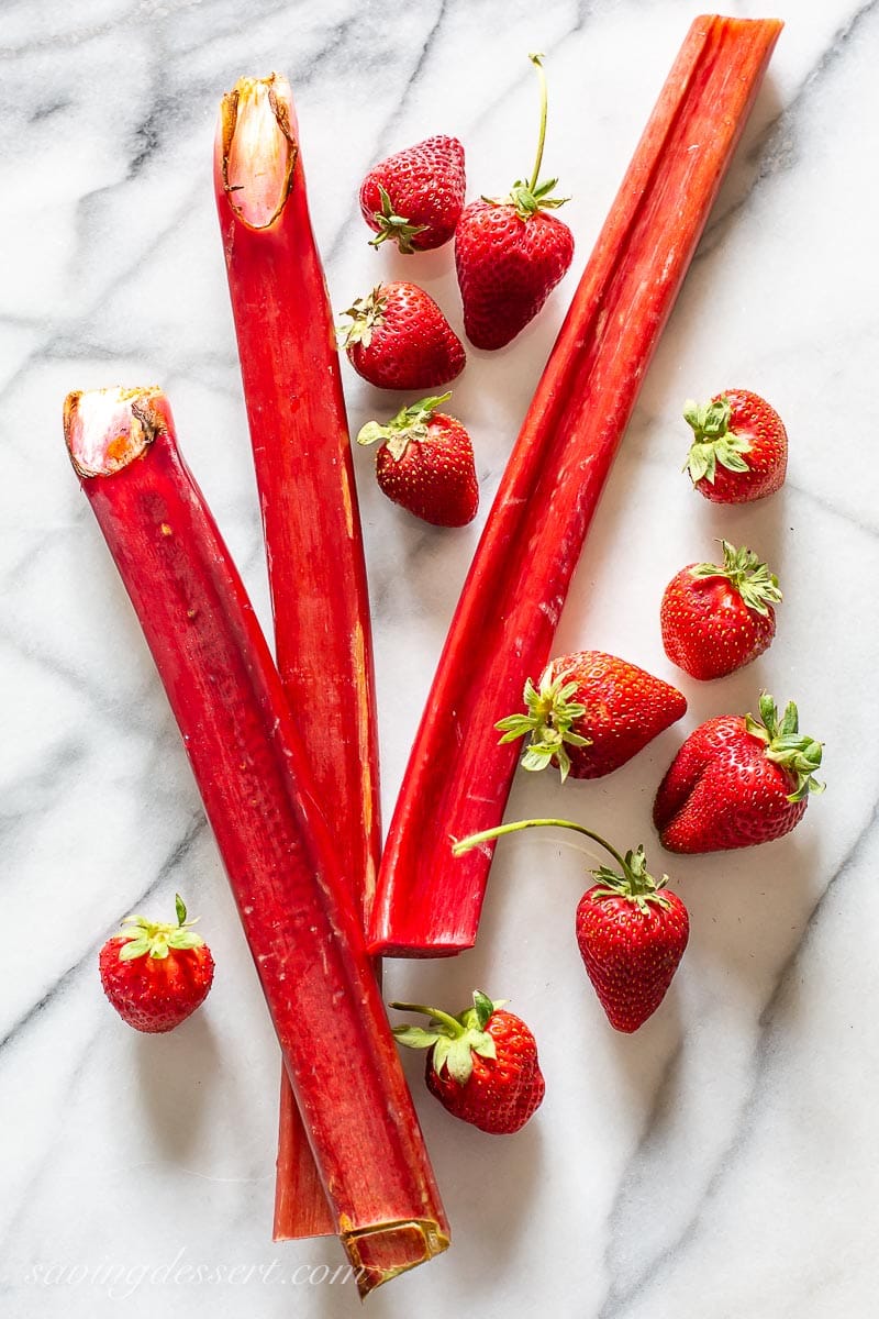 Rhubarb stalks with fresh strawberries on a marble slab