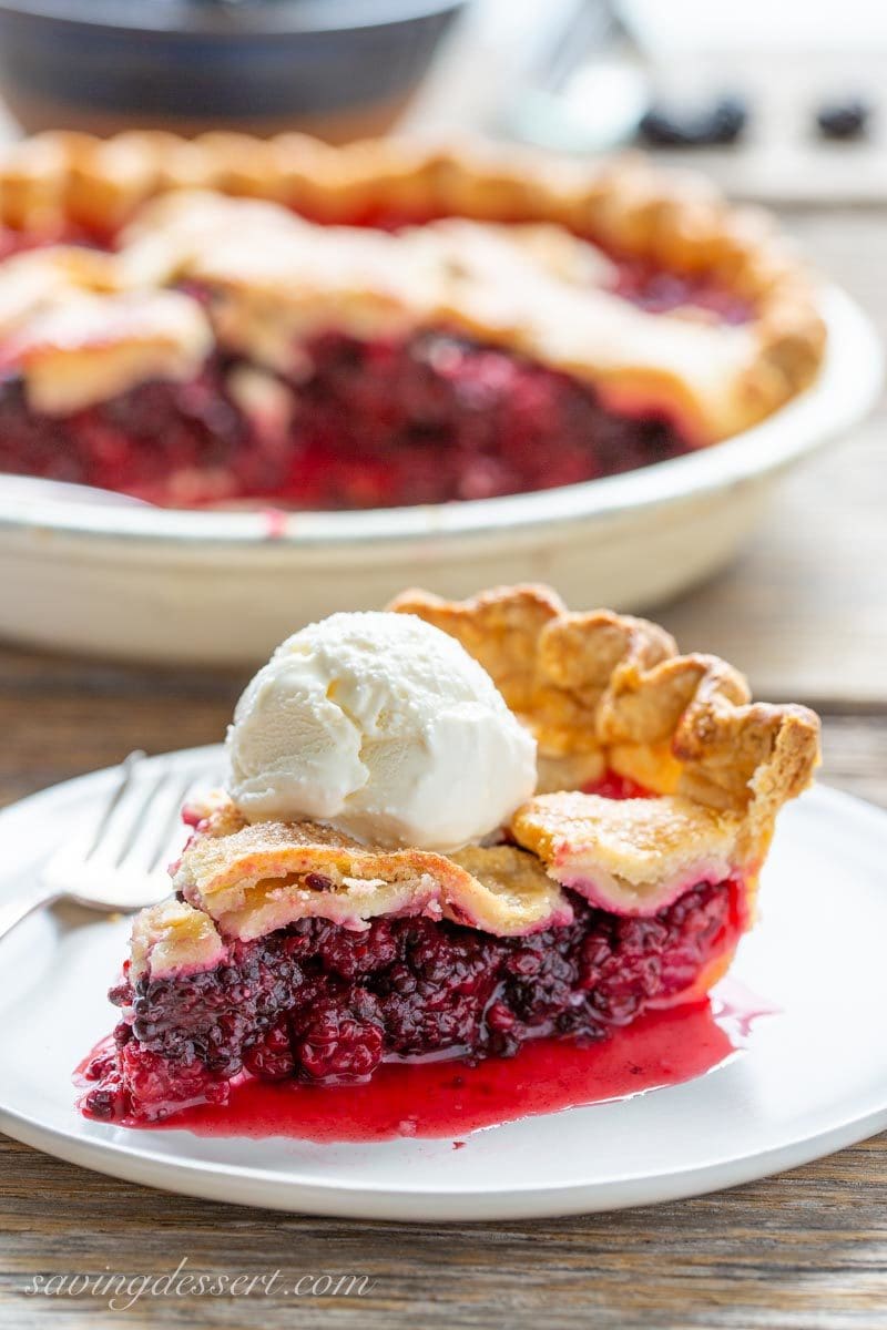 a slice of very juicy blackberry pie with a scoop of ice cream on top