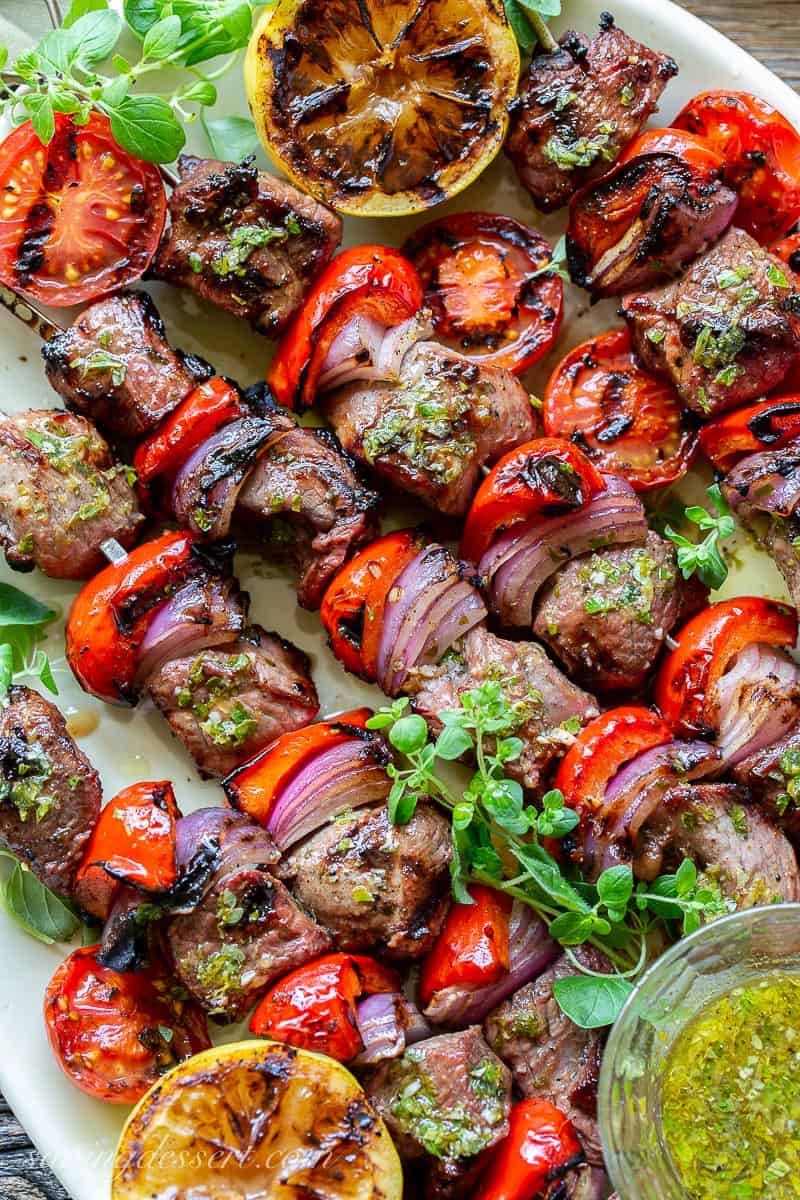 Lamb Souvlaki skewers on a platter with a lemon garlic olive oil sauce and fresh oregano