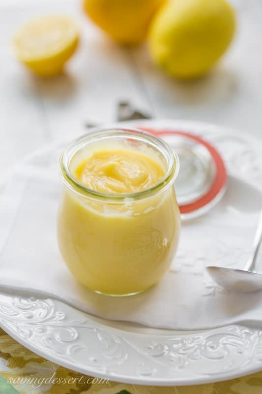 A jar of homemade lemon curd on a plate with a spoon