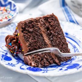 A slice of chocolate birthday cake on a blue plate with a fork cut a site out.