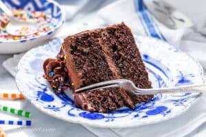 A slice of chocolate birthday cake on a blue plate with a fork cut a site out.