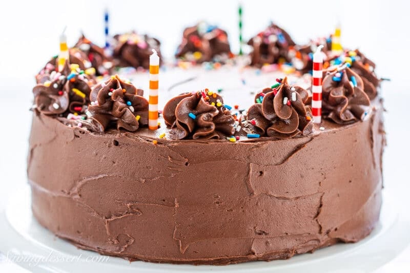 A side view of a chocolate cake with swirls of chocolate on top decorated with colorful sprinkles and birthday candles.