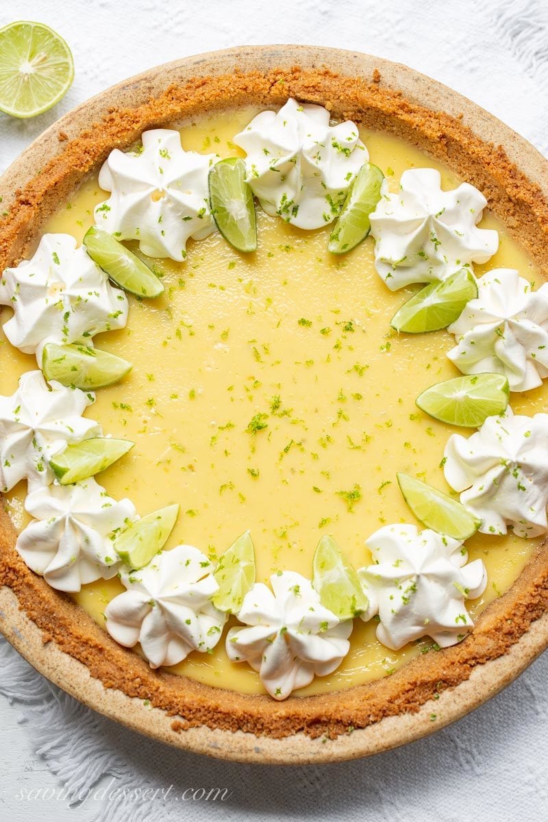 An overhead view of a key lime pie garnished with whipped cream and lime wedges